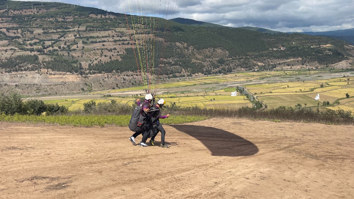 پرواز تندم پاراگلایدر؛ خلبان و مسافر در حال دویدن روی زمین و آماده برای بلند شدن